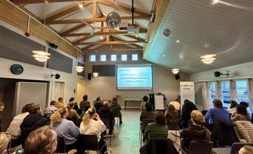 en gruppe mennesker som sitter i et rom og ser på en skjerm