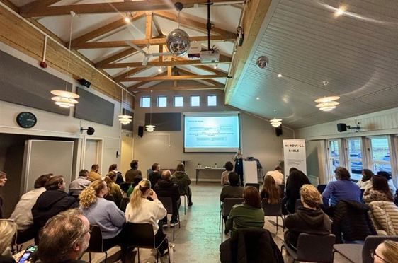 en gruppe mennesker som sitter i et rom og ser på en skjerm