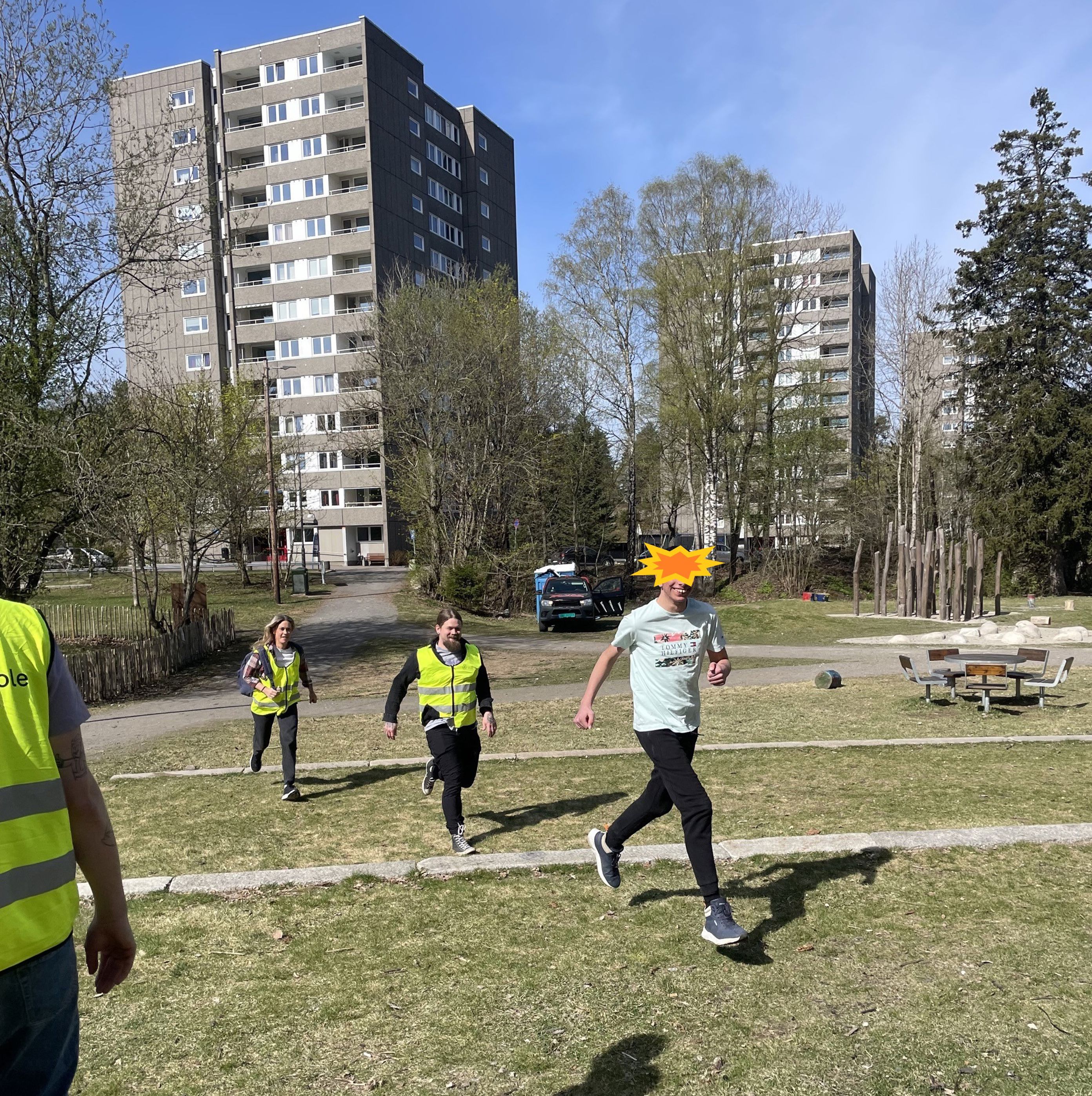 En gruppe mennesker som løper på en gresslette med bygninger i bakgrunnen